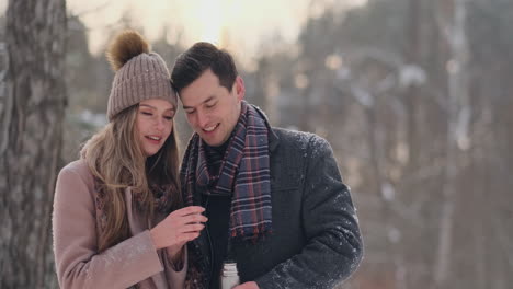 Beautiful-and-stylish-couple-man-and-woman-hipsters-in-a-coat-and-scarf-drink-tea-from-a-thermos-in-the-winter-forest-after-a-walk.-Love-story